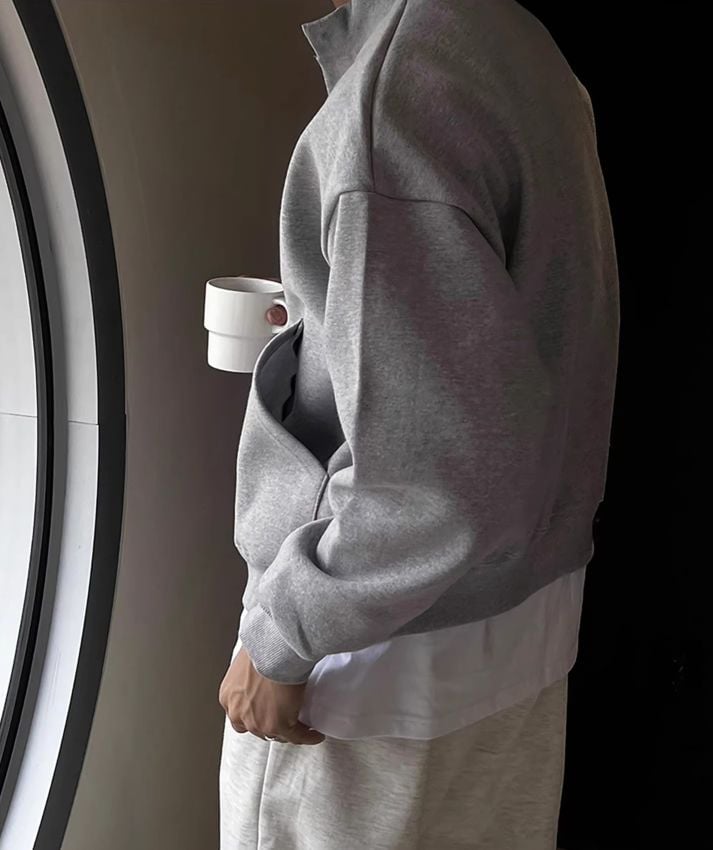 グレーのスタンドカラーカーディガンを着用し、白いマグカップを持つ男性の横姿。サイドの立体的な大きなポケットとインナーの白Tシャツ。