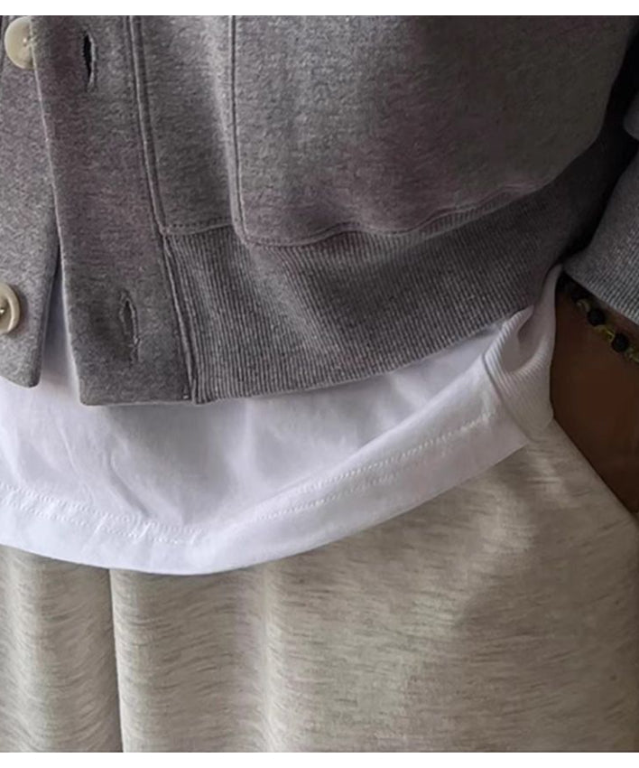 グレーのスタンドカラーカーディガンの裾リブと、インナーの白いTシャツ、ライトグレーのパンツが重なるレイヤード部分のアップ。