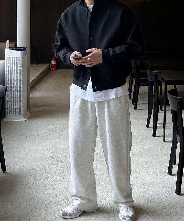 ブラックのスタンドカラーカジュアルカーディガンを着用し、スマートフォンを両手で持つ男性の全身コーディネート姿。