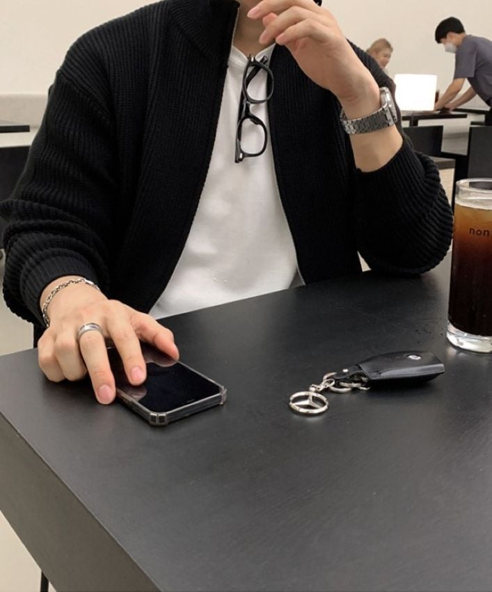 ブラックのジップアップニットカーディガンを着用し、黒いテーブルの上のスマートフォンに手を添える男性の手元と上半身のアップ。