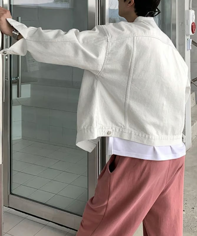 ホワイトのバンドカラーデニムジャケットを着用し、ガラス扉を開けようとする男性の後ろ姿。ドロップショルダーと裾のシルエット。