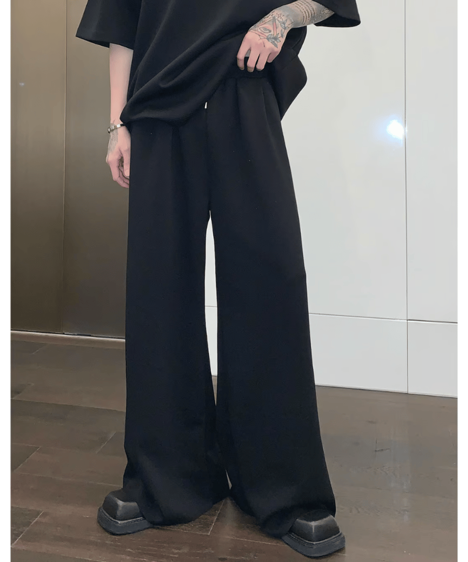 ブラックのセットアップのスウェットワイドパンツに黒のボリュームシューズを合わせ、左手をポケットに入れて立つ男性の腰から下のスタイリング。