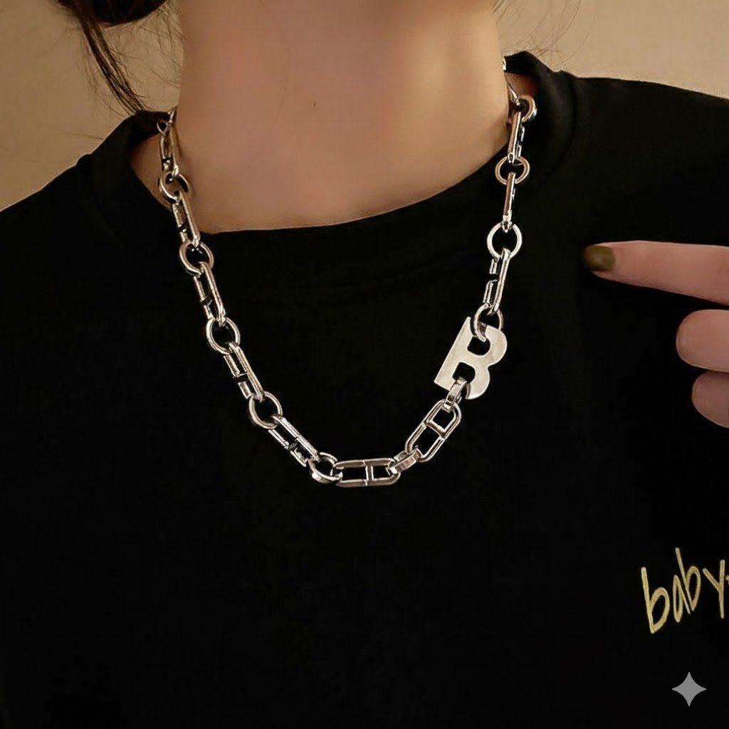 黒いTシャツを着用した人の首元に飾られた、アルファベットのBの形をしたチャーム付きのシルバーチェーンネックレスの写真。