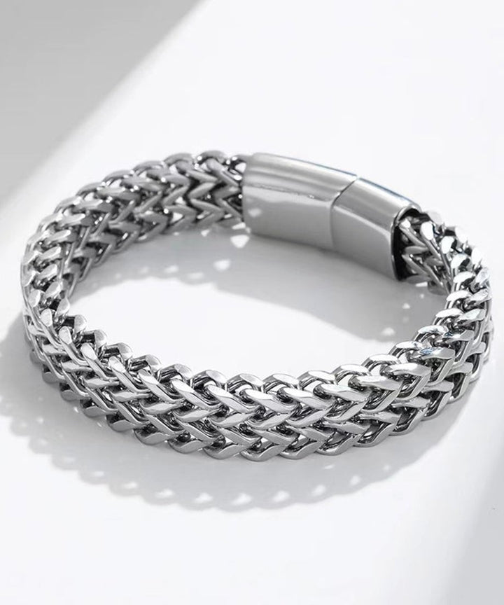 白い大理石風の背景の上で円状に置かれたメタリックシルバーのブレスレット。差し込み式のシリンダー型バックルディテールが鮮明に見える物撮り画像。