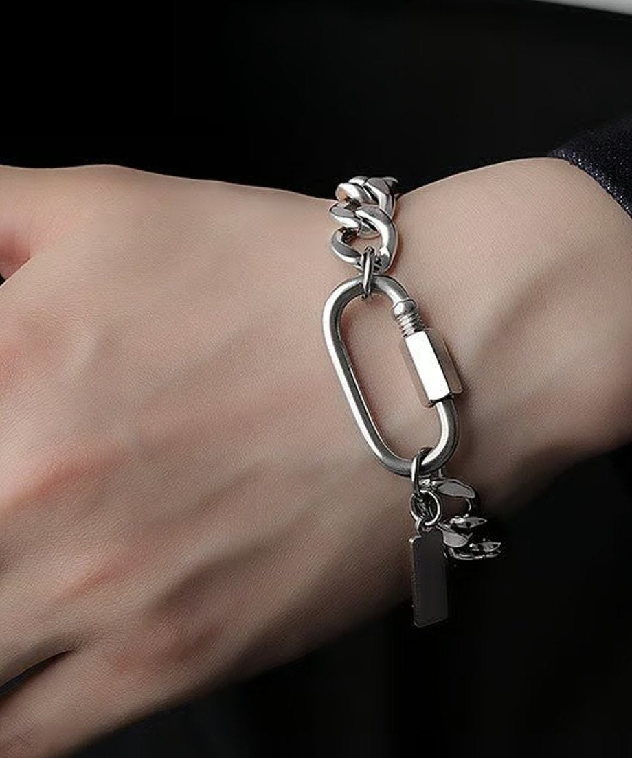 黒いトップスを着用した手首に、存在感のあるカラビナモチーフとキヘイチェーンを組み合わせたインダストリアルリンクチェーンブレスレットを着用したスタイリッシュなスナップ。
