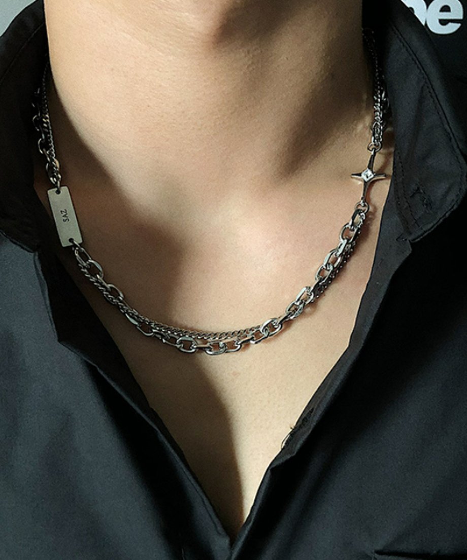 ネックラインが少し開いた黒シャツのスタイリング。メタルプレートに刻まれた「SAZ」の文字が覗き、見る角度によって表情を変えるアシンメトリーデザインの魅力を捉えたカット。