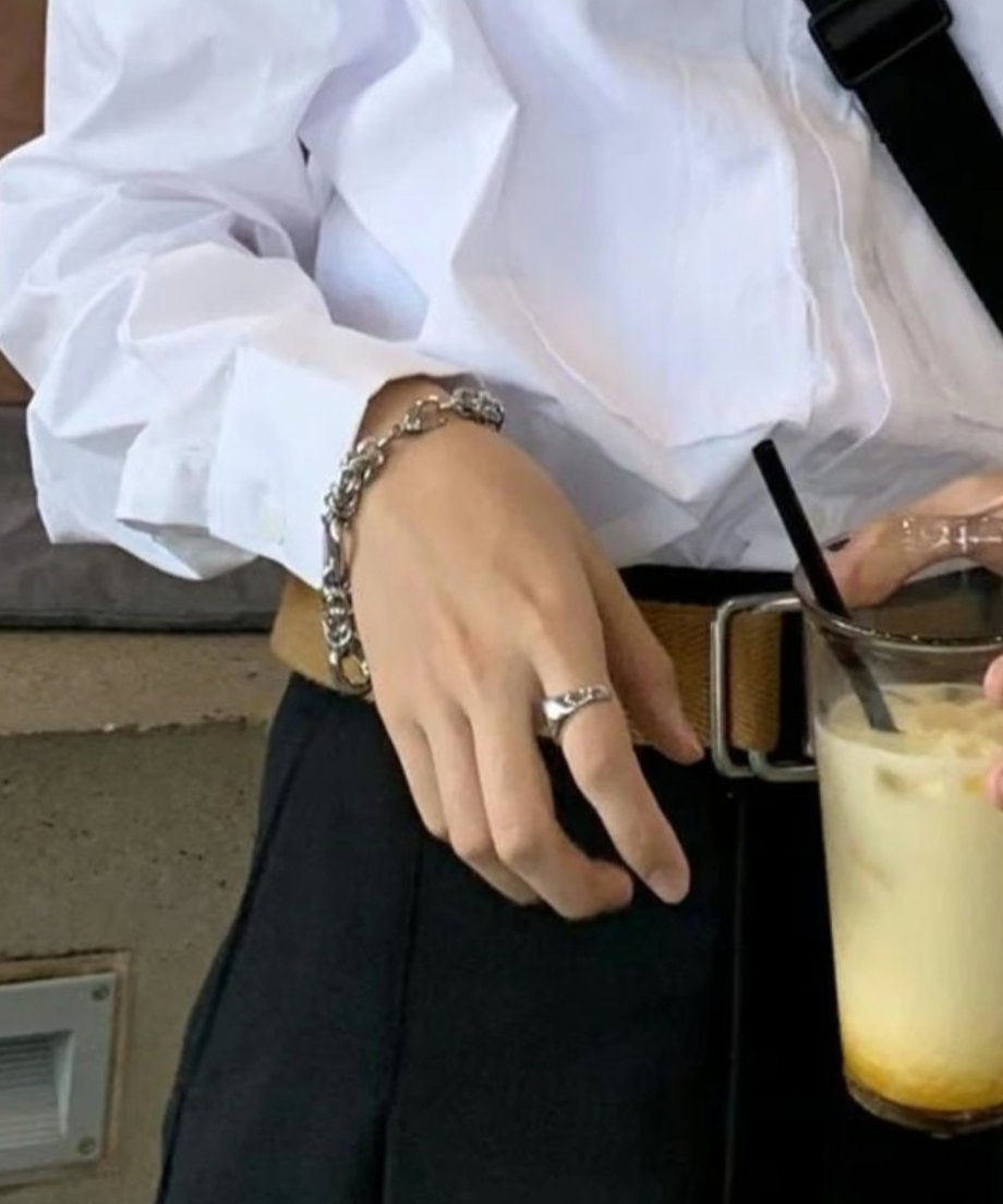 白シャツに黒のボトムスを合わせた男性が、カフェでドリンクを持ち佇む手元スナップ。清潔感のあるキレイめストリートファッションに、武骨なブレスレットがエッジを添える着用画像。