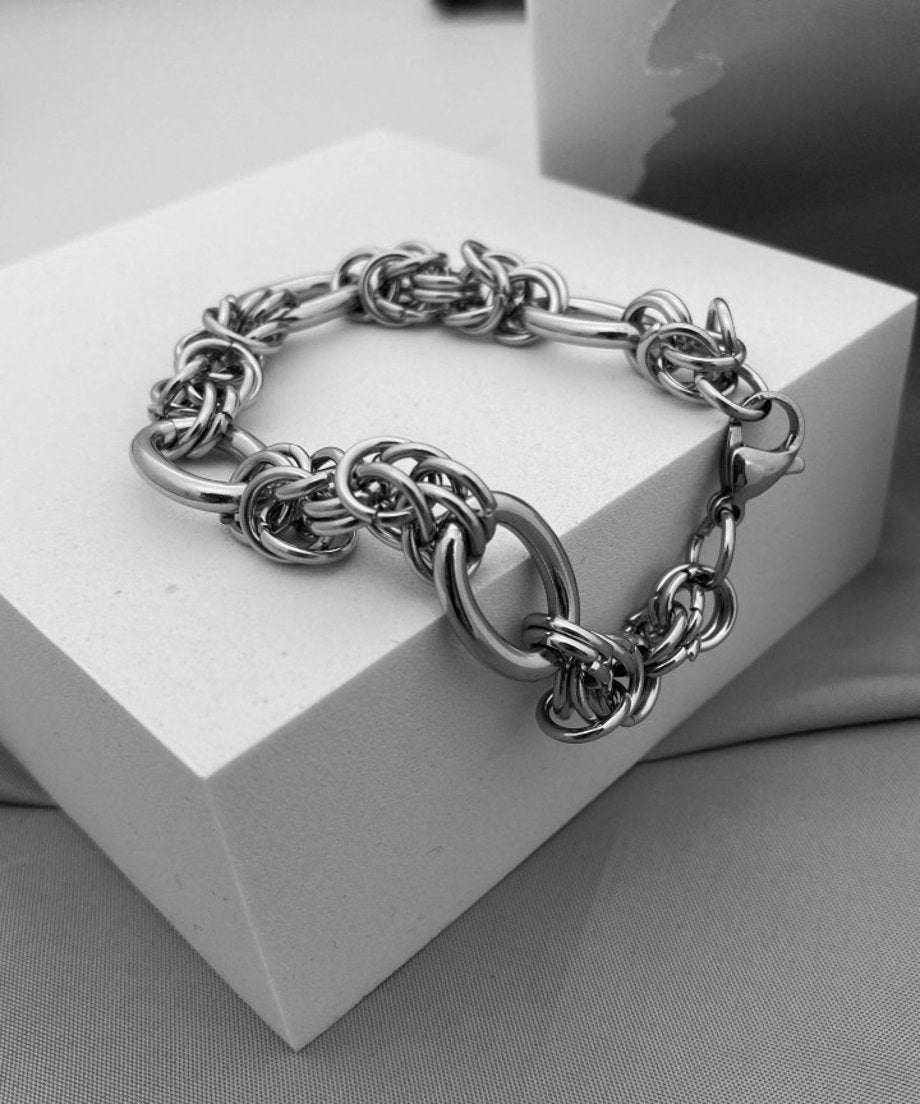 白いディスプレイブロックの上に立体的に置かれたブレスレットのモノトーン調画像。カニカンパーツと緻密なメイル編みのディテールを際立たせたカット。