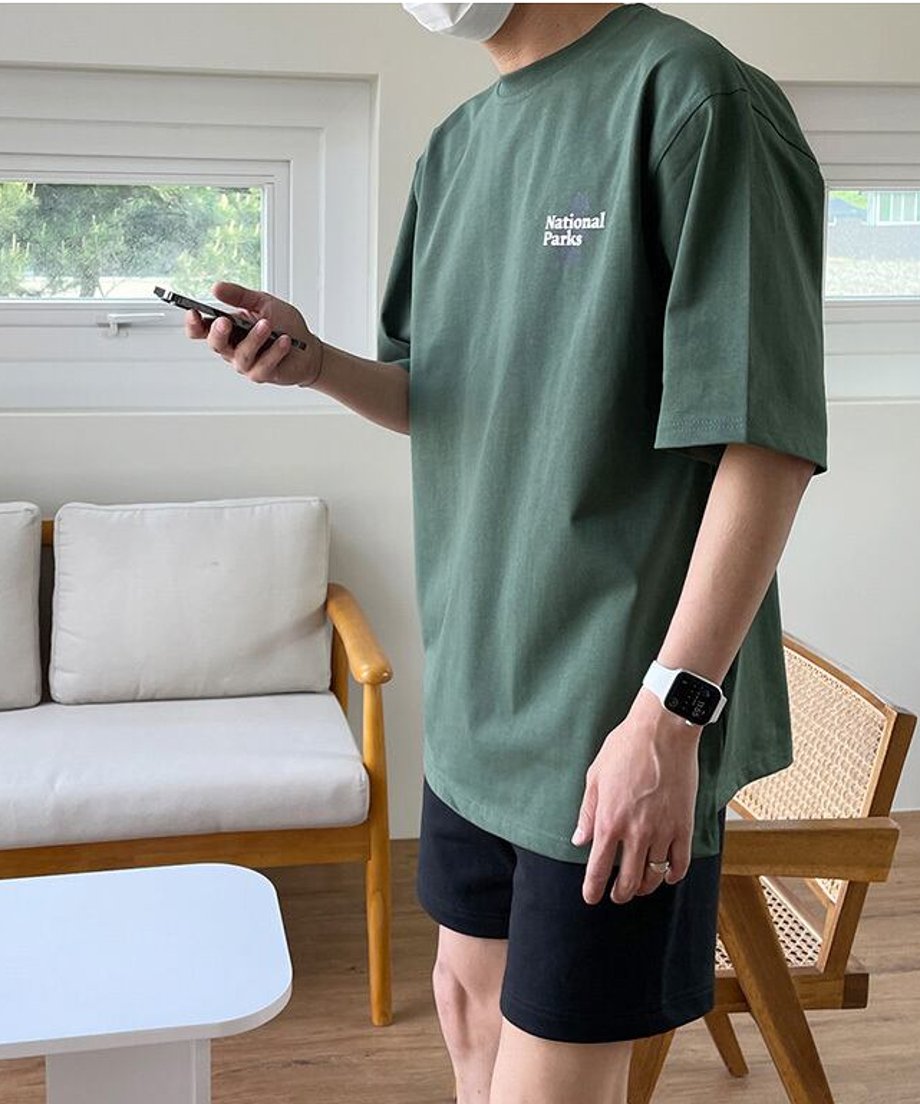 スマートフォンを操作しながら、少し斜めを向いて佇む男性のアップカット。深みのあるグリーンの色味が、室内の柔らかな光の中で上品なこなれ感を醸し出しているビジュアル。