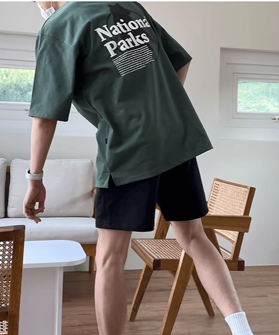 動きの中で軽く後ろにステップを踏むようなアクティブなポーズの男性。背中のグラフィックと全体のルーズなサイズ感が、軽快でスポーティな印象を与えるカット。