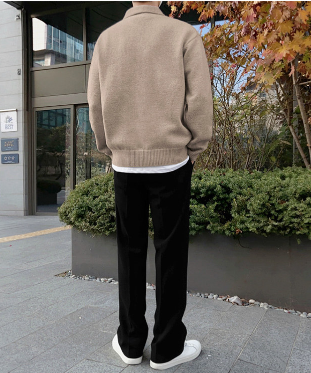 カーキのポロニットセーターに黒いスラックス、白いスニーカーを合わせ、建物に向かって立っている人物の後ろ姿。