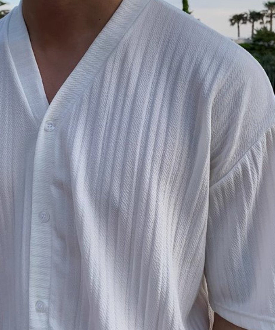 縦プリーツの凹凸感が引き立つ、ホワイトのセットアップのトップスシャツを着用した男性の胸元ディテールアップ。