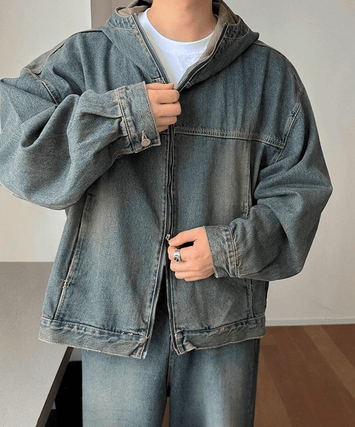 オーバーサイズデニムセットアップのジャケットのフロントジッパーに手をかけ、シルバーのリングをはめた手元がアクセントになる男性のチェストアップ。