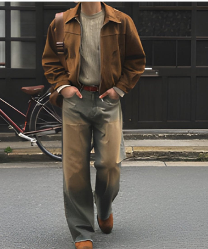 自転車が置かれたレトロな街並みのなかを、両手をポケットに入れてこちらへ向かって歩いてくる男性の全身スタイリング。ブラウン、アイボリー、ウォッシュドデニムのカラーバランスが秀逸なシティカジュアル。