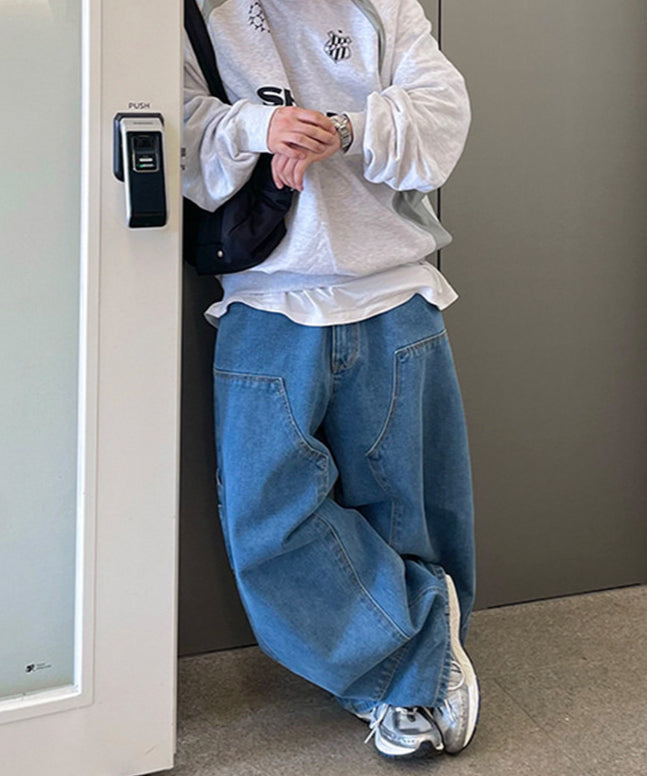グレー杢のスウェットにブルーのワイドパネルデニムパンツを合わせ、ドアに寄りかかっている人物のフロントカット。