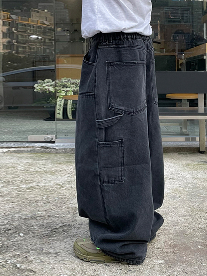 白いTシャツにブラックのワイドパネルデニムパンツ、オリーブグリーンのスニーカーを穿いた人物の横からのカット。