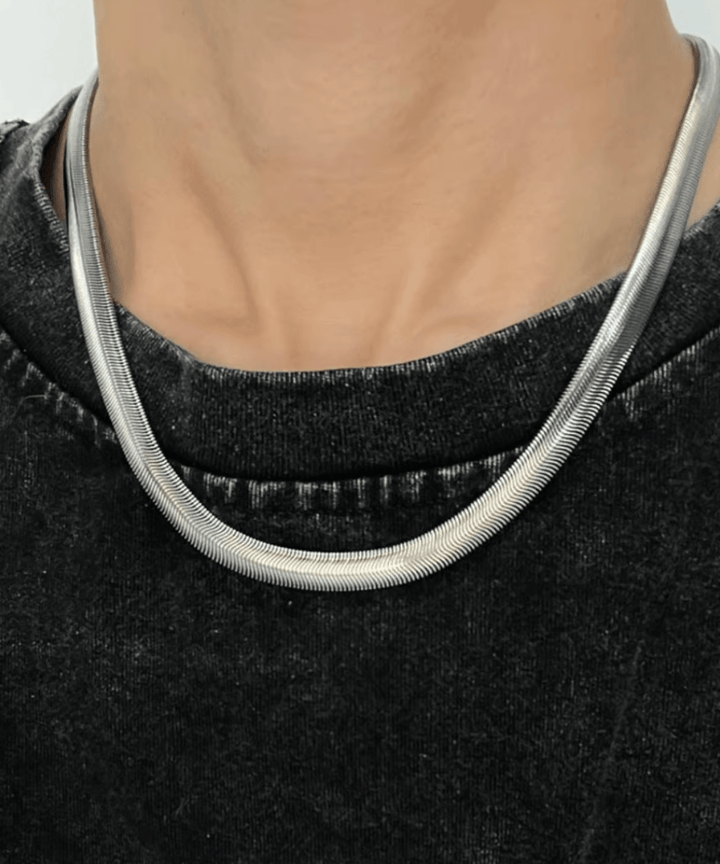 ウォッシュ加工が施されたヴィンテージライクな黒のTシャツの丸首に沿うように、シルバーのスネークチェーンネックレスを着用した男性のフロントショット。