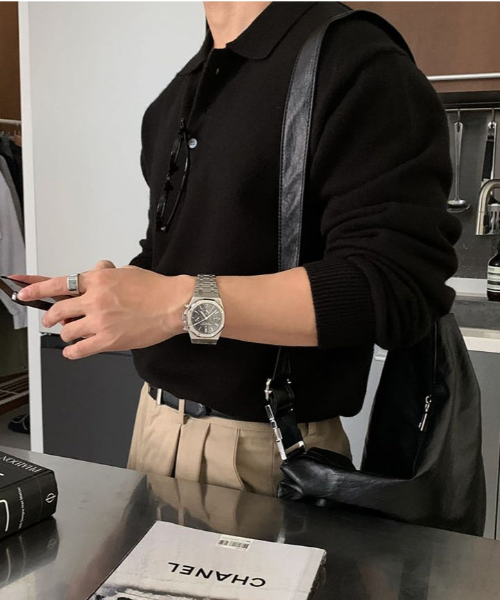 ベージュのワイドパンツにブラックのポロニットをタックインし、黒のショルダーバッグを背負ってスマートフォンを操作する人物を斜めから捉えたカット。
