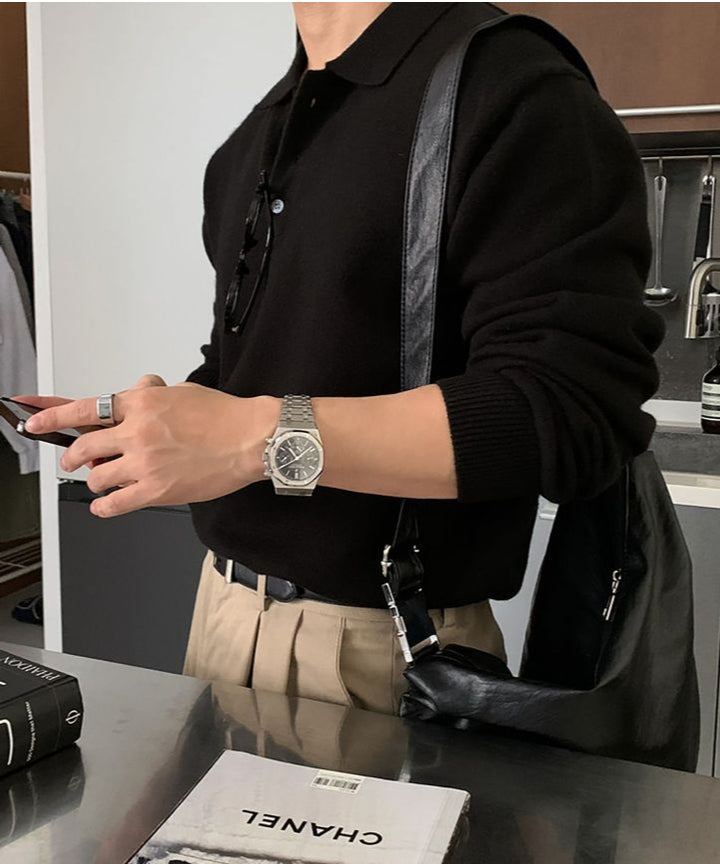 ベージュのワイドパンツにブラックのポロニットをタックインし、黒のショルダーバッグを背負ってスマートフォンを操作する人物を斜めから捉えたカット。