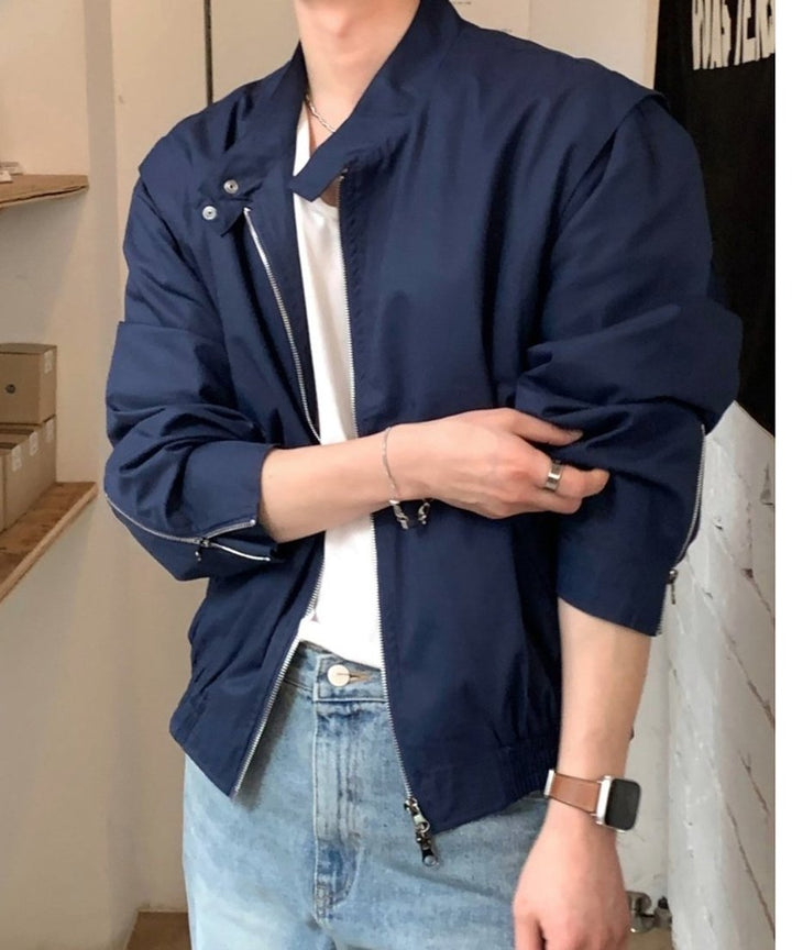 白のTシャツと淡いブルーのウォッシュドデニムに、ネイビーのワイドブルゾンを羽織った男性のフロントクローズアップ。袖口のジップを開けて腕を捲り上げた、こなれ感のあるスタイリング。