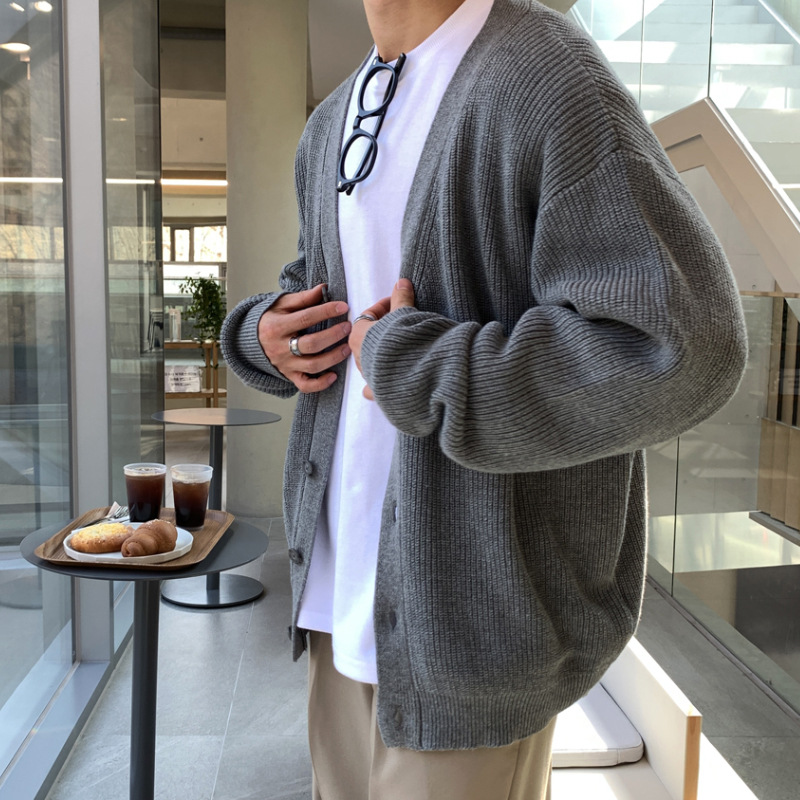 グレーのオーバーサイズカーディガンを羽織った人物のサイドルック。両手を前立て部分に添え、ボリュームのある袖のたるみや、リブ編みの美しい立体感が際立つアングル。