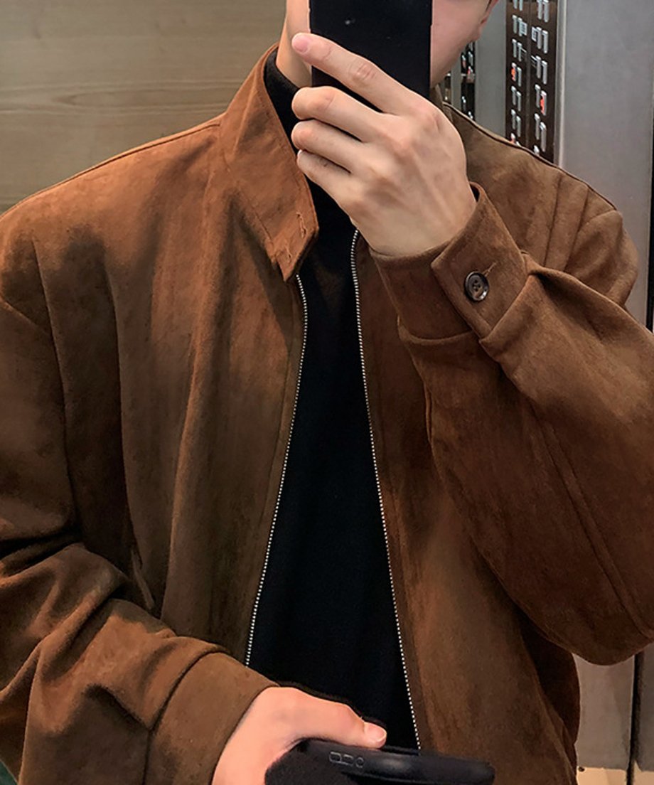 ブラウンのブルゾンを着用した男性が、スマートフォンを鏡にかざして自撮り（セルフィー）をする、エレベーター内での胸元クローズアップショット。
