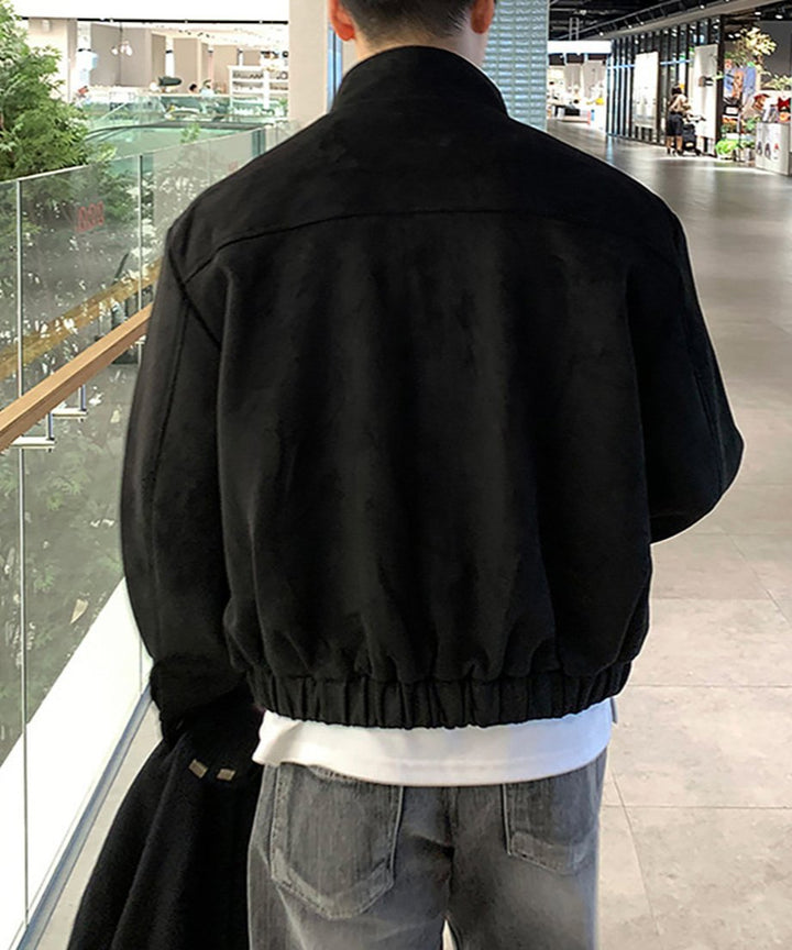 ブラックのフェイクスエードブルゾンを着用した男性のバックスタイル。インナーの白Tシャツが裾から少し覗く、計算されたレイヤードと、ゆったりとした背面のシルエット。