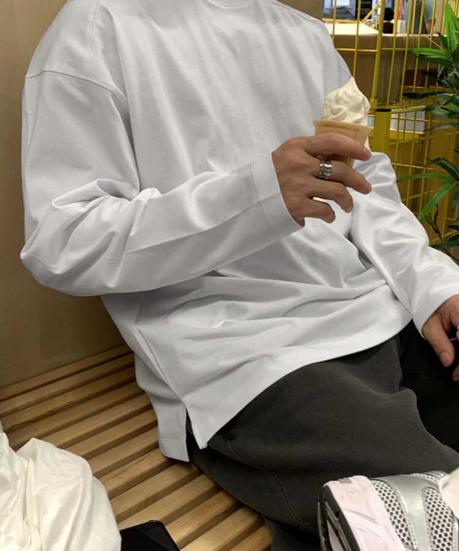 ベンチにリラックスして座る男性の、ドロップショルダーから流れる美しい袖のボリューム感を捉えたミドルカット。