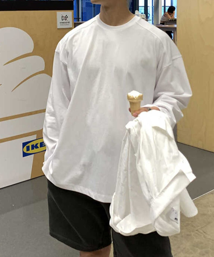 ホワイトのオーバーサイズロンTにチャコールグレーのショーツを合わせた男性のフロントカット。右手にはアイスクリームを持ち、左手には白いシャツをラフに抱えた、キャッチーで清潔感のあるデイリーカジュアル。