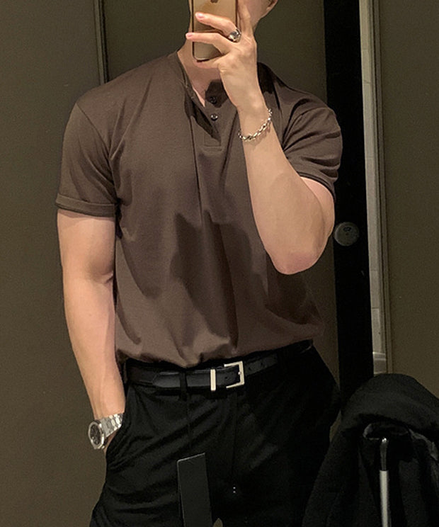 コーヒーのヘンリーネックニットTシャツに黒のレザーベルト、黒のスラックスを合わせ、スマートフォンで鏡越しに自撮りをする人物のクローズアップ。