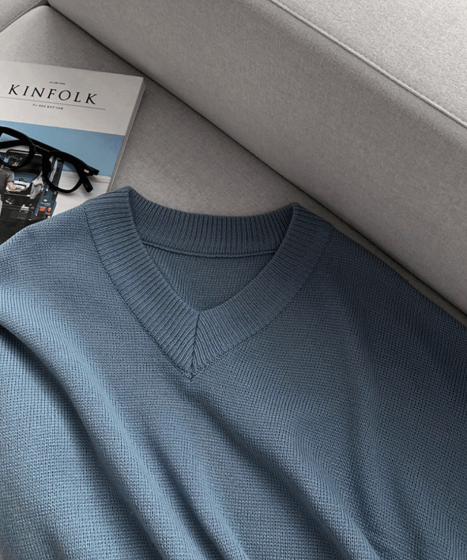 ソファーの上に無造作に置かれたライトブルーのセーター。傍らに「KINFOLK」の雑誌と黒縁メガネが添えられた、こなれ感のある物撮りカット。