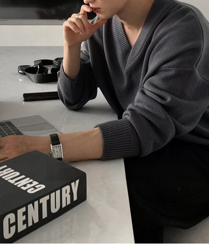 アイアングレーのVネックセーターを着用し、デスクでノートPCに向かいながら考え事をする男性の、大人のリラックス感漂う上品な横顔カット。