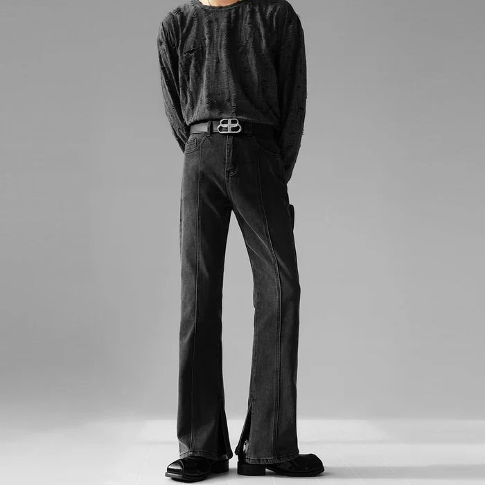 センターシームと裾スリットが特徴のブラックフレアデニムパンツを着用した男性の全体正面。ベルトを着用。