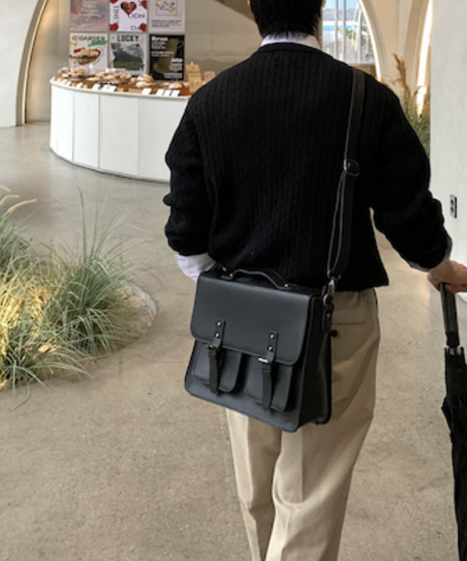 ブラックのケーブルカーディガンにベージュのスラックスを合わせ、黒のレザーサッチェルバッグを斜め掛けして歩く男性の後ろ姿のスタイリングカット。