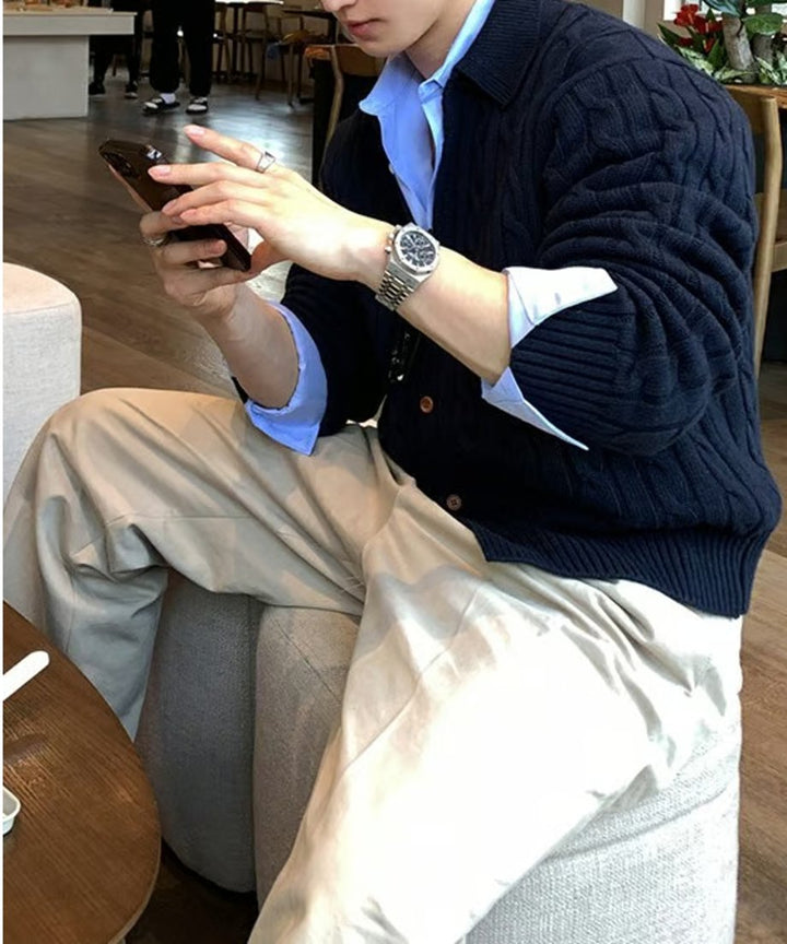 カフェのソファ席に座り、スマートフォンを操作する男性のサイドからのスタイリングカット。ネイビーのカーディガンの袖から覗くブルーのシャツのカフスやシルバーの腕時計が洗練された印象を与える。