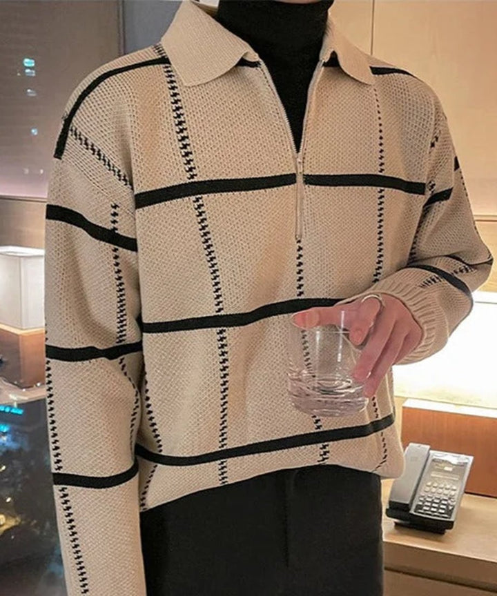ベージュのブロックチェック柄ハーフジップポロニットに、黒のボトムスを合わせた男性の正面アップ写真。