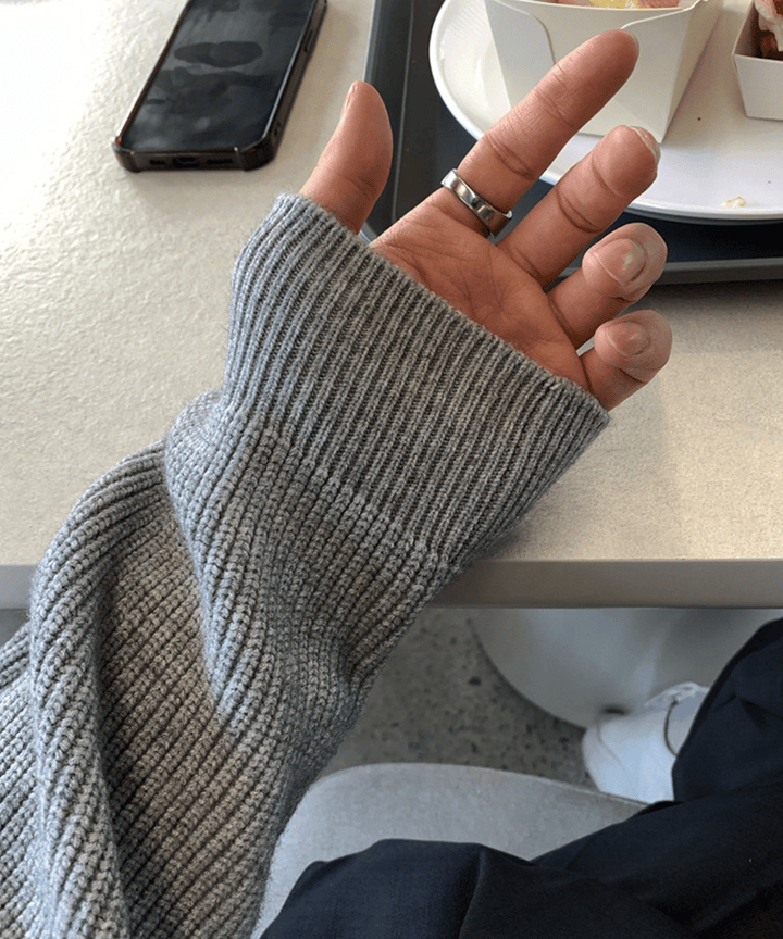 グレーのリブニットの袖口から覗く男性の手のアップ。手の甲にかかる長めの細リブ仕様と、人差し指に光る太めのシルバーリングの質感。