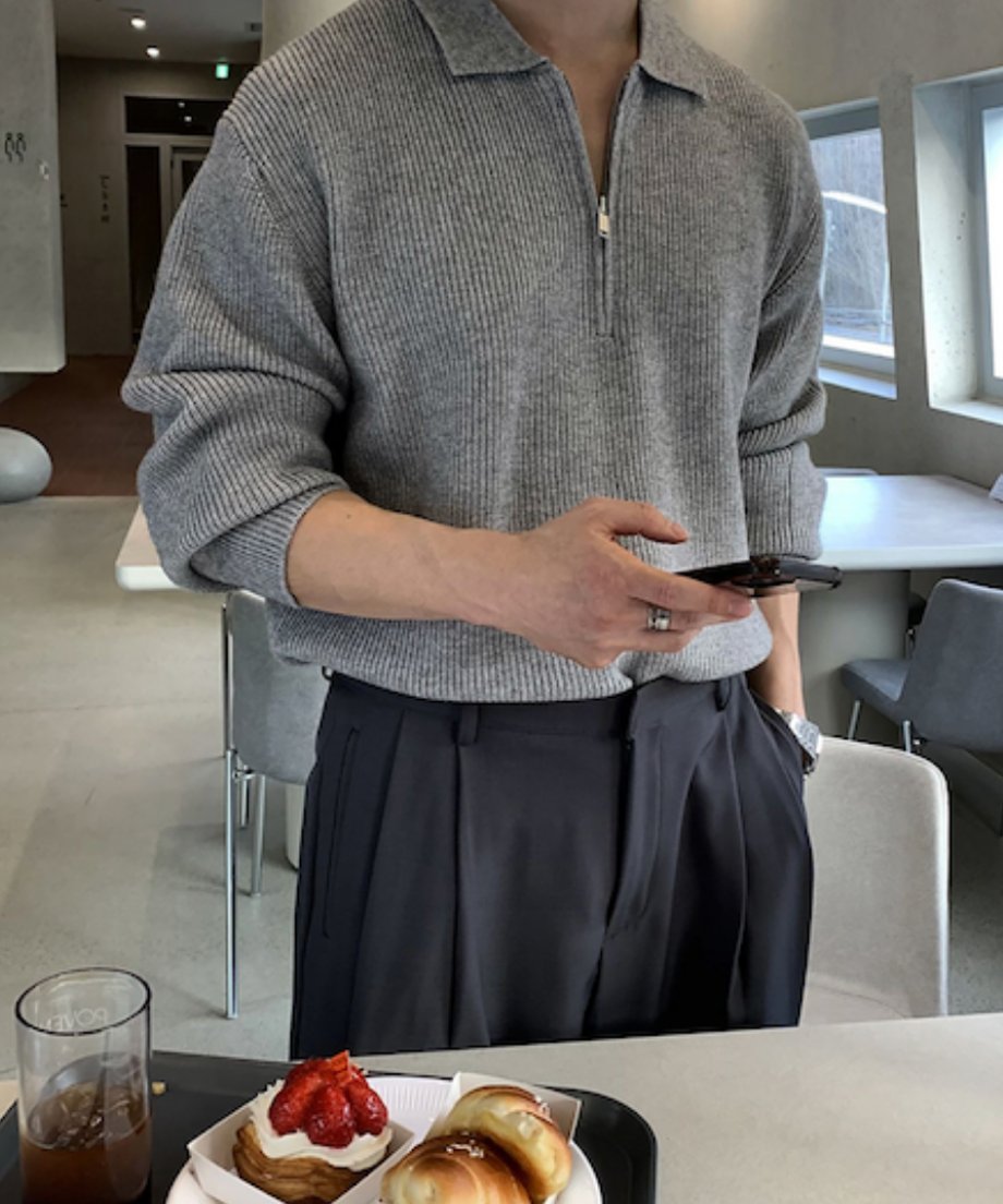 グレーのハーフジップ襟付きリブニットを着用した男性のフロントショット。手前にはカフェのトレイに載ったストロベリーデニッシュやクロワッサン、アイスコーヒーがボケて写っている、ライフスタイル感溢れるカット。