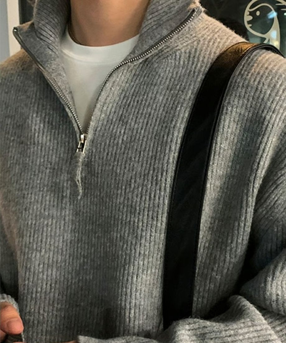 グレーのリブニットトップスの胸元と、シルバーの滑らかなジップ、インナーの白Tシャツのレイヤードを強調したデティールアップカット。