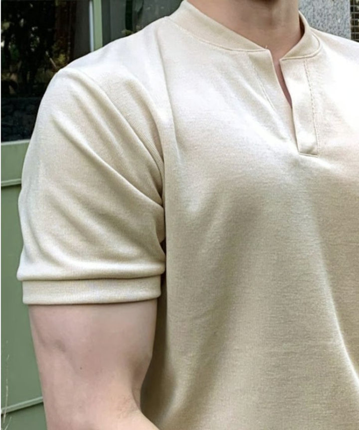 ニットポロを着用した男性の、右肩から二の腕、首元にかけての超クローズアップ画像。ボタンのない特徴的なVネックラインの仕立てや、袖口のリブ編み、きめ細かくしなやかなニット生地の質感が伝わる一枚。
