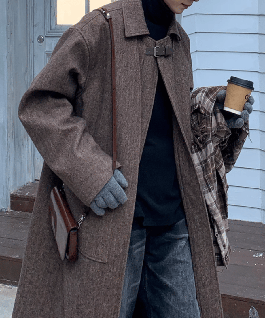 コーヒーを手に持った動きのあるポーズのカット。腕を動かした際に見える袖のボリューム感や、フロントの比翼仕立て（ボタンが隠れる仕様）のミニマルなデザインが伝わるスタイリッシュな一枚。