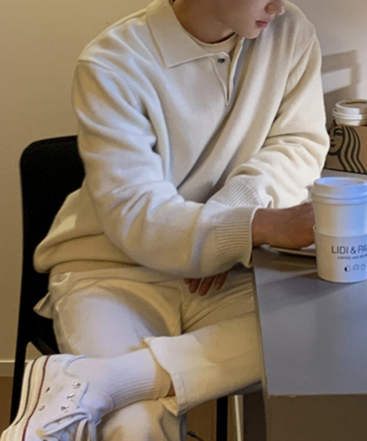 デスクに向かって椅子に座り、足を組んで作業をしている男性のサイドカット。白Tシャツを首元から覗かせたレイヤードと、全体をホワイトでまとめた爽やかな日常に馴染む画像。