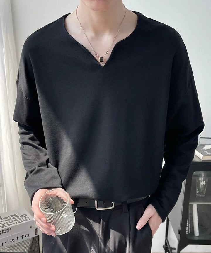 黒のVネック長袖カットソーを着用し、右手にデザインガラスのコップを持った男性のポーズ写真。