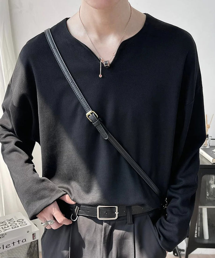 Vネックの黒の長袖Tシャツを着用し、黒いレザーのスクエアショルダーバッグを斜め掛けした男性のポーズ写真。