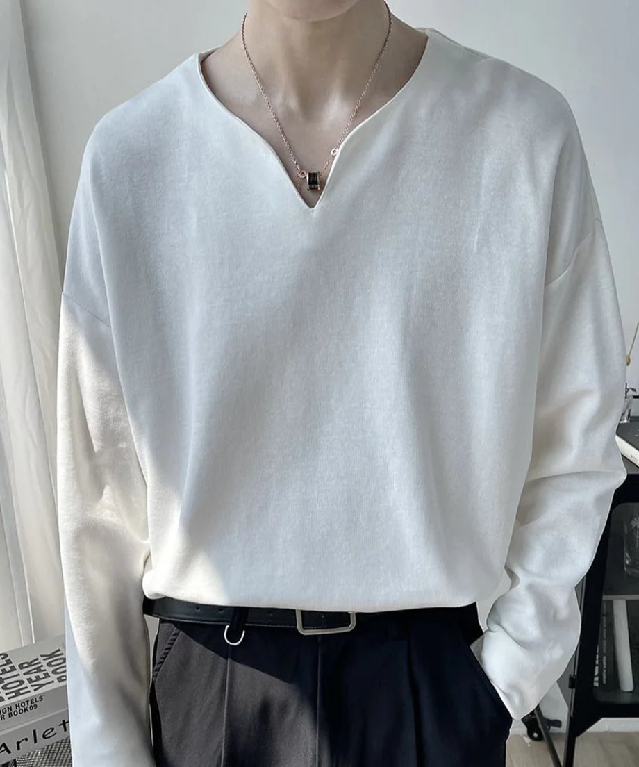浅いVネックのホワイトの長袖カットソーを黒のボトムスにタックインした男性の正面アップ写真。