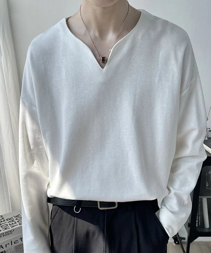 浅いVネックのホワイトの長袖カットソーを黒のボトムスにタックインした男性の正面アップ写真。