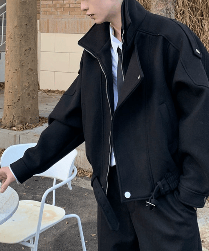 ブラック着用。屋外のテラス席横で、少し斜めを向いた男性のショット。ジップをやや開けて、インナーのシャツとネクタイを覗かせた、大人のこなれ感を感じさせる一枚。