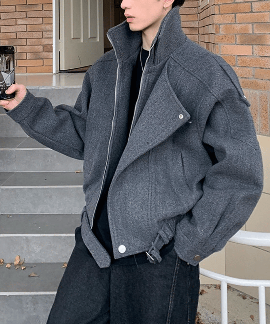 階段の手すりに寄りかかり、スマホを持つ男性のミドルショット。ワイドなブラックデニムとブルゾンのショート丈が織りなす、今っぽいAラインのバランス感が伝わる一枚。
