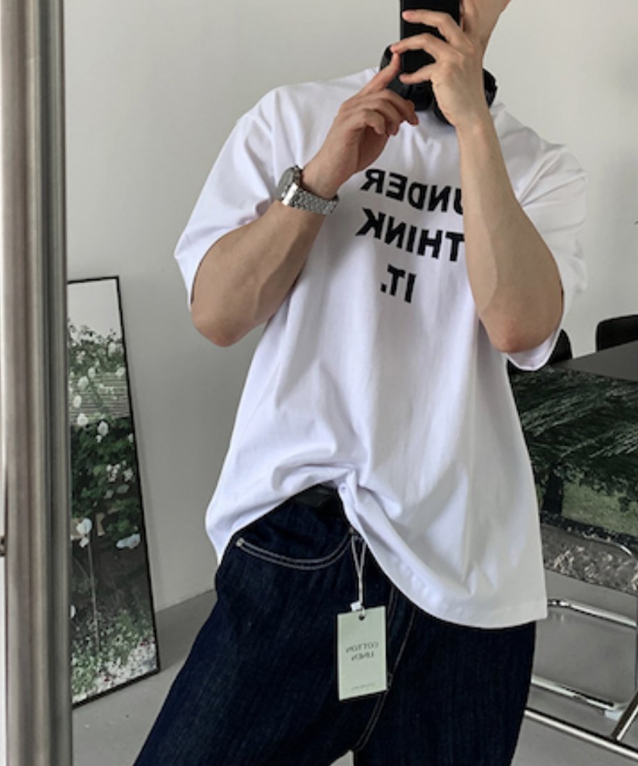 「UNDER THINK IT.」の黒いグラフィックロゴが際立つホワイトTシャツのアップカット。首元に掛けられた黒いヘッドフォンにスマホを持ったスタイリッシュな一枚。
