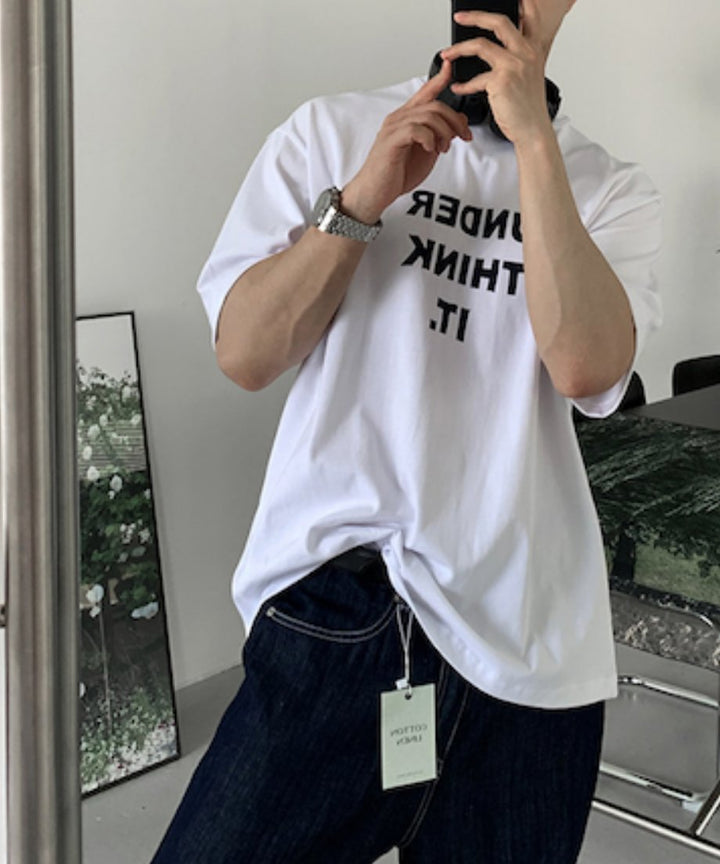 「UNDER THINK IT.」の黒いグラフィックロゴが際立つホワイトTシャツのアップカット。首元に掛けられた黒いヘッドフォンにスマホを持ったスタイリッシュな一枚。